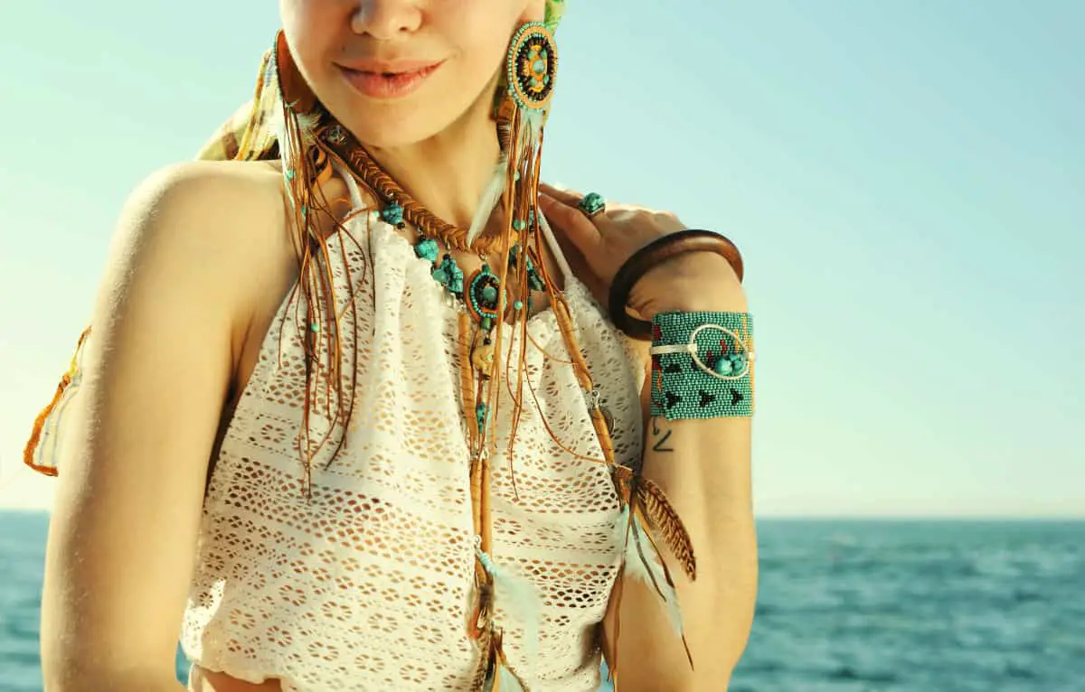 Female neck and hand with boho bracelets and necklace near sea, fashion portrait, white lace tank top, sunny backlit